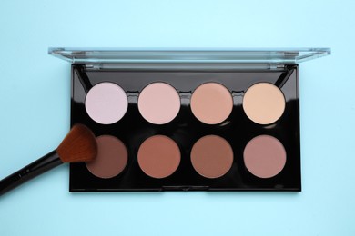 Photo of Colorful contouring palette with brush on light blue background, top view. Professional cosmetic product