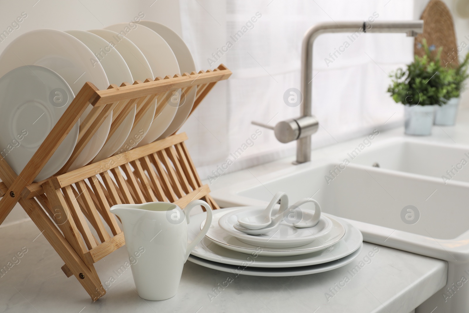 Photo of Drying rack with clean dishes on light marble countertop near sink in kitchen