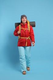 Photo of Smiling young woman with backpack walking on light blue background. Active tourism