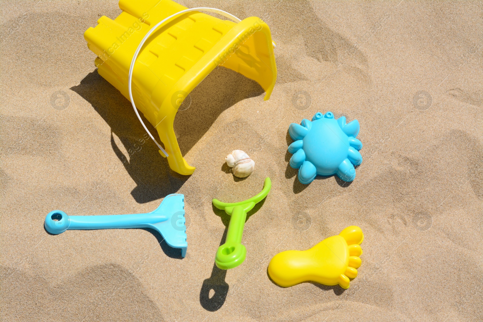 Photo of Bright plastic bucket, rake and shovel on sand. Beach toys