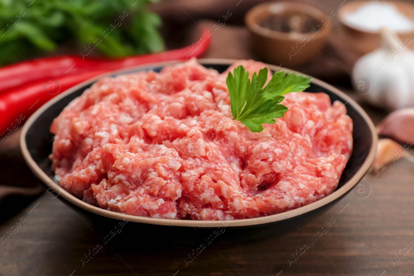 Photo of Bowl of raw fresh minced meat with parsley on wooden table, closeup