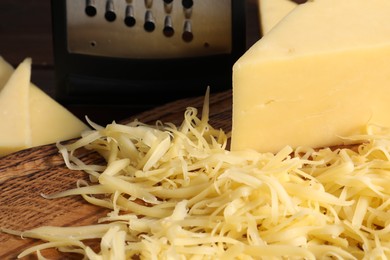 Photo of Grated and whole piece of cheese on wooden board, closeup