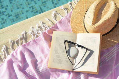 Photo of Pink blanket with hat, sunglasses and book near outdoor swimming pool on sunny day, flat lay
