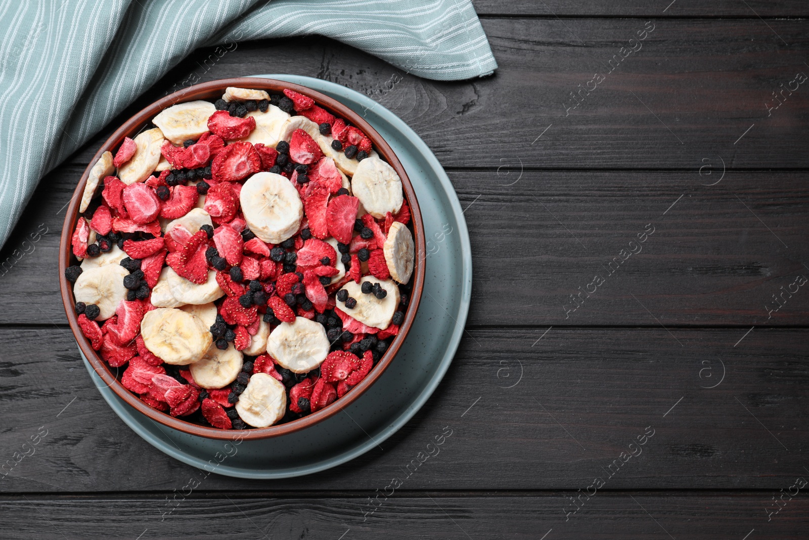 Photo of Bowl of different freeze dried fruits on wooden table, top view. Space for text