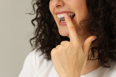 Photo of Young woman applying whitening strip on her teeth against light grey background, closeup. Space for text