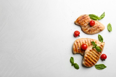 Tasty grilled chicken fillets with cherry tomatoes and green basil on light grey table, flat lay. Space for text