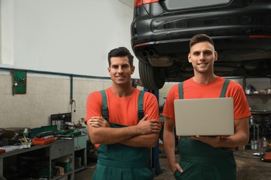 Photo of Mechanics with laptop near lifted car at automobile repair shop