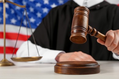 Photo of Judge with gavel at white wooden table against flag of United States, closeup