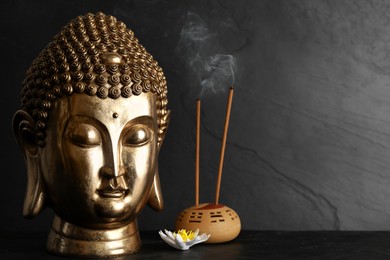 Buddha statue, lotus flower and incense sticks on black table. Space for text
