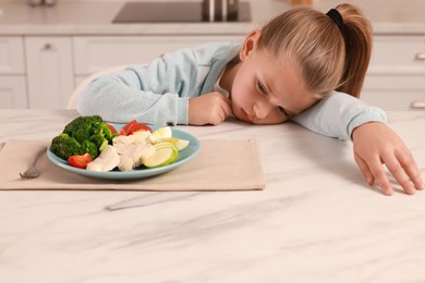 Photo of Cute little girl refusing to eat dinner in kitchen