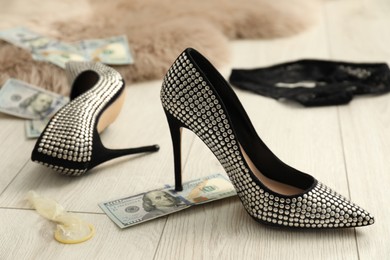 Photo of Prostitution concept. High heeled shoes, condom and dollar banknote on floor indoors, closeup