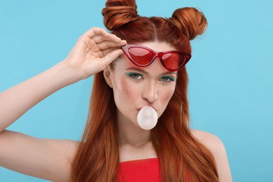 Photo of Portraitbeautiful woman in sunglasses blowing bubble gum on light blue background