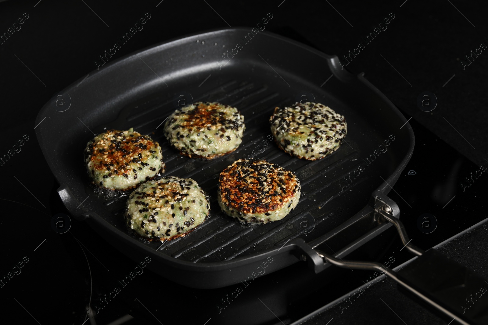 Photo of Cooking tasty vegan cutlets with sesame in grill pan on cooktop, closeup