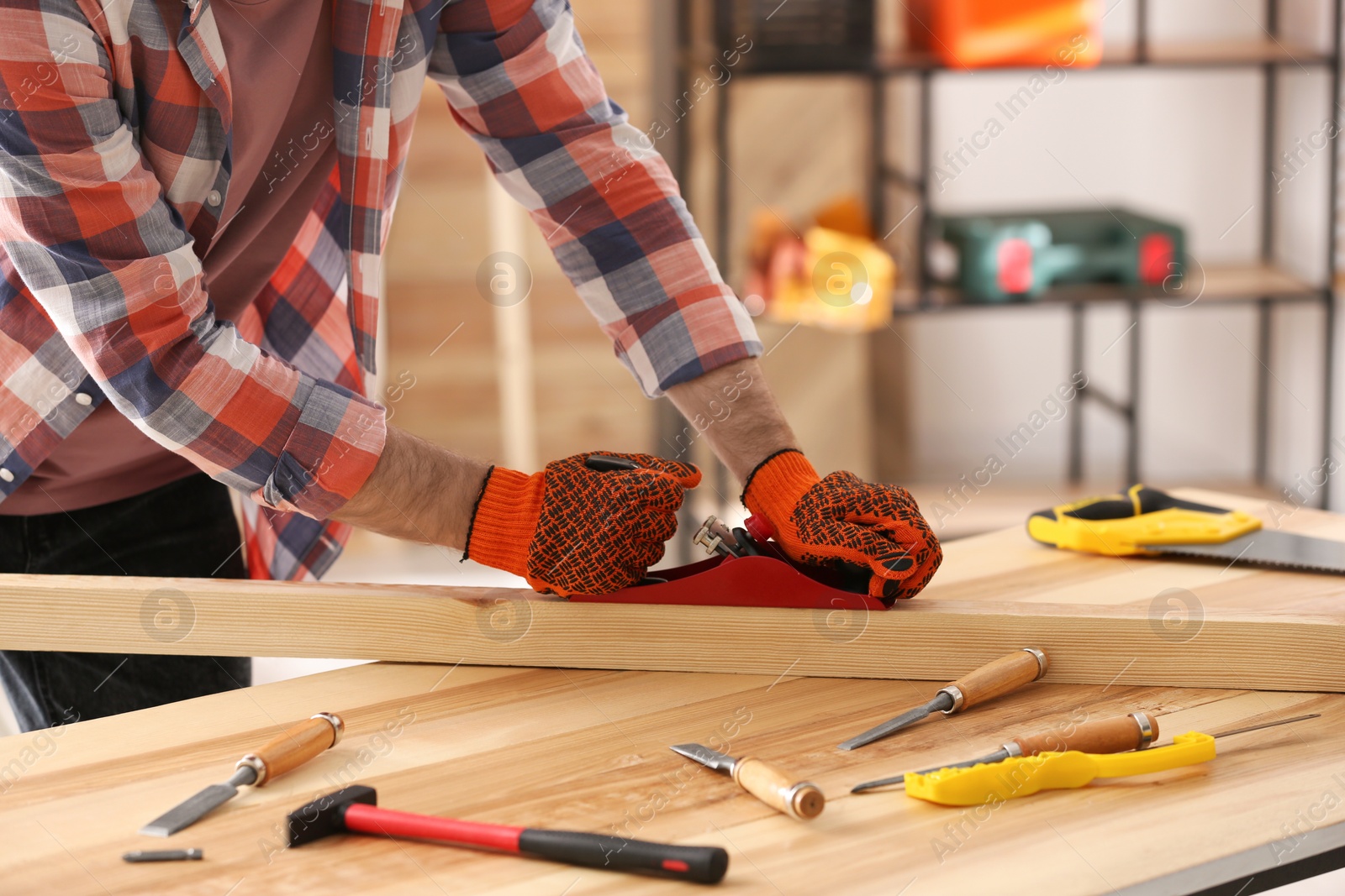 Photo of Carpenter shaping wooden bar with hand plane at table in workshop, closeup