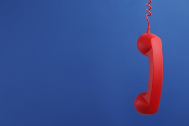 Photo of Red corded telephone handset hanging on blue background, space for text. Hotline concept