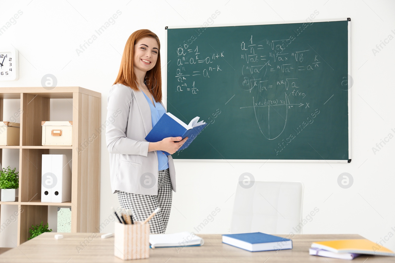 Photo of Beautiful young teacher explaining math formulas written on blackboard in classroom