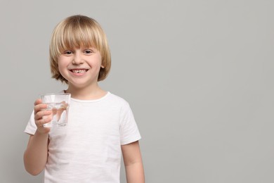 Photo of Happy little boy holding glass of fresh water on light grey background. Space for text