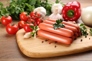 Photo of Fresh raw vegetarian sausages with parsley and vegetables on wooden table