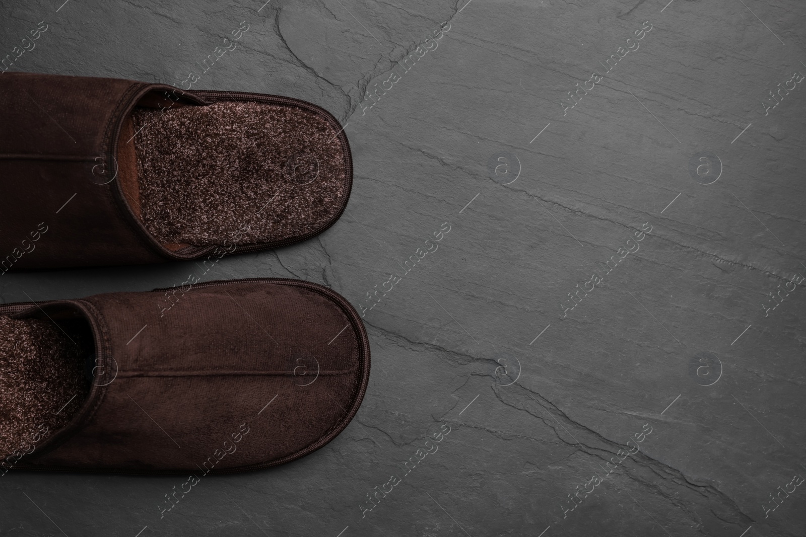 Photo of Pair of brown slippers on dark grey floor, top view. Space for text