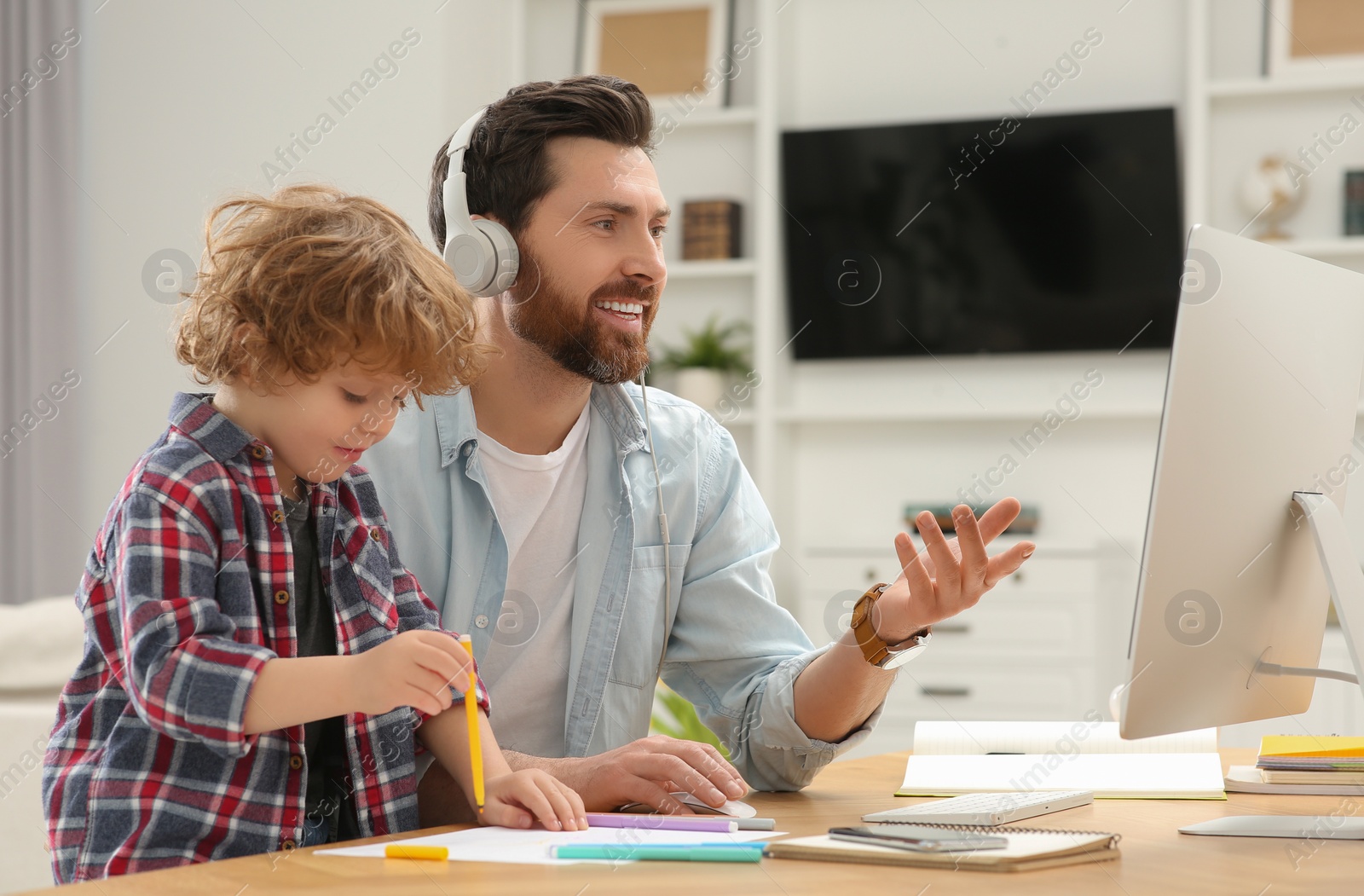 Photo of Man working remotely at home. Father having video chat with colleagues while his son drawing at desk