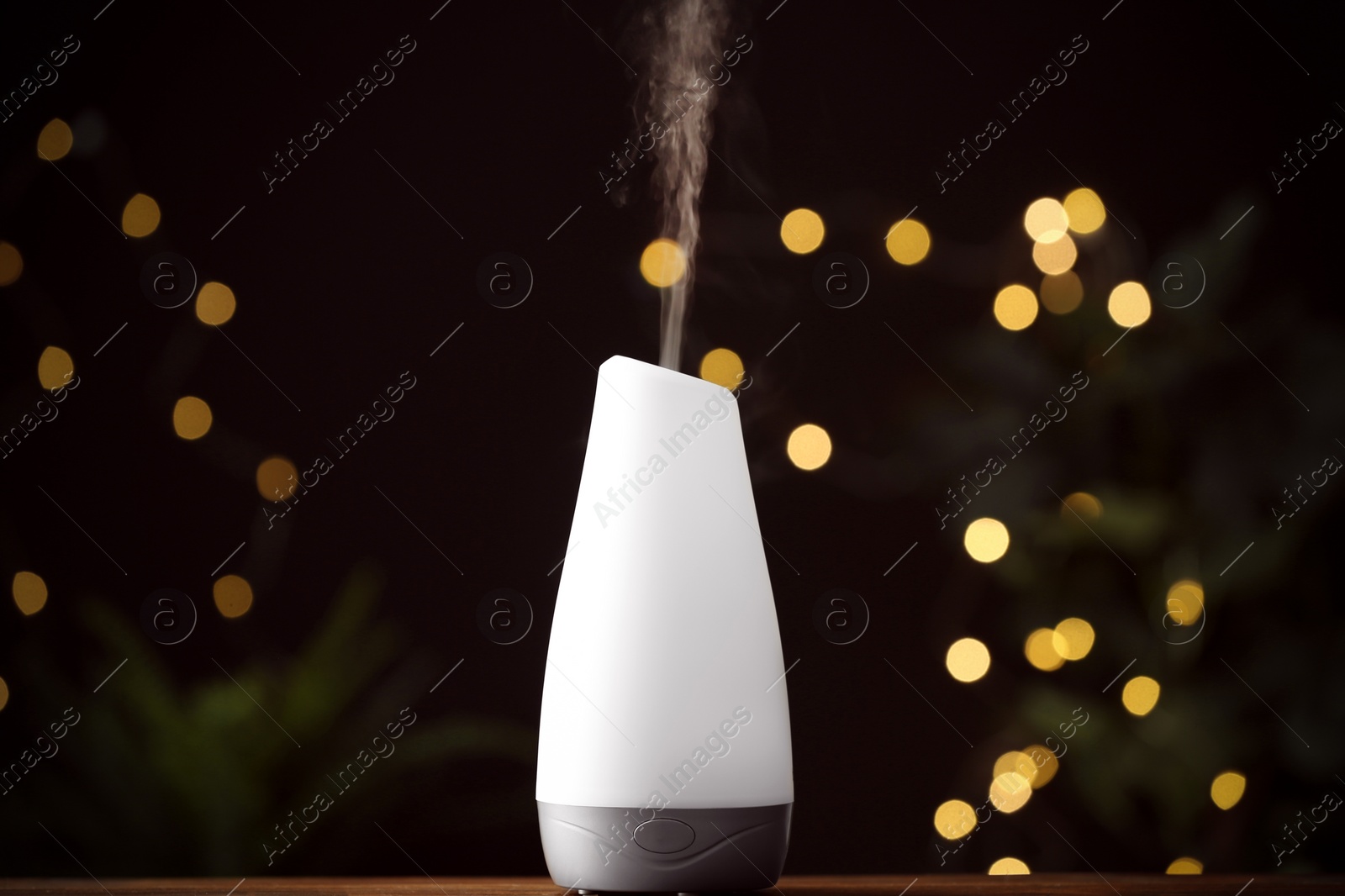 Photo of Modern aroma humidifier on wooden table against blurred lights, space for text