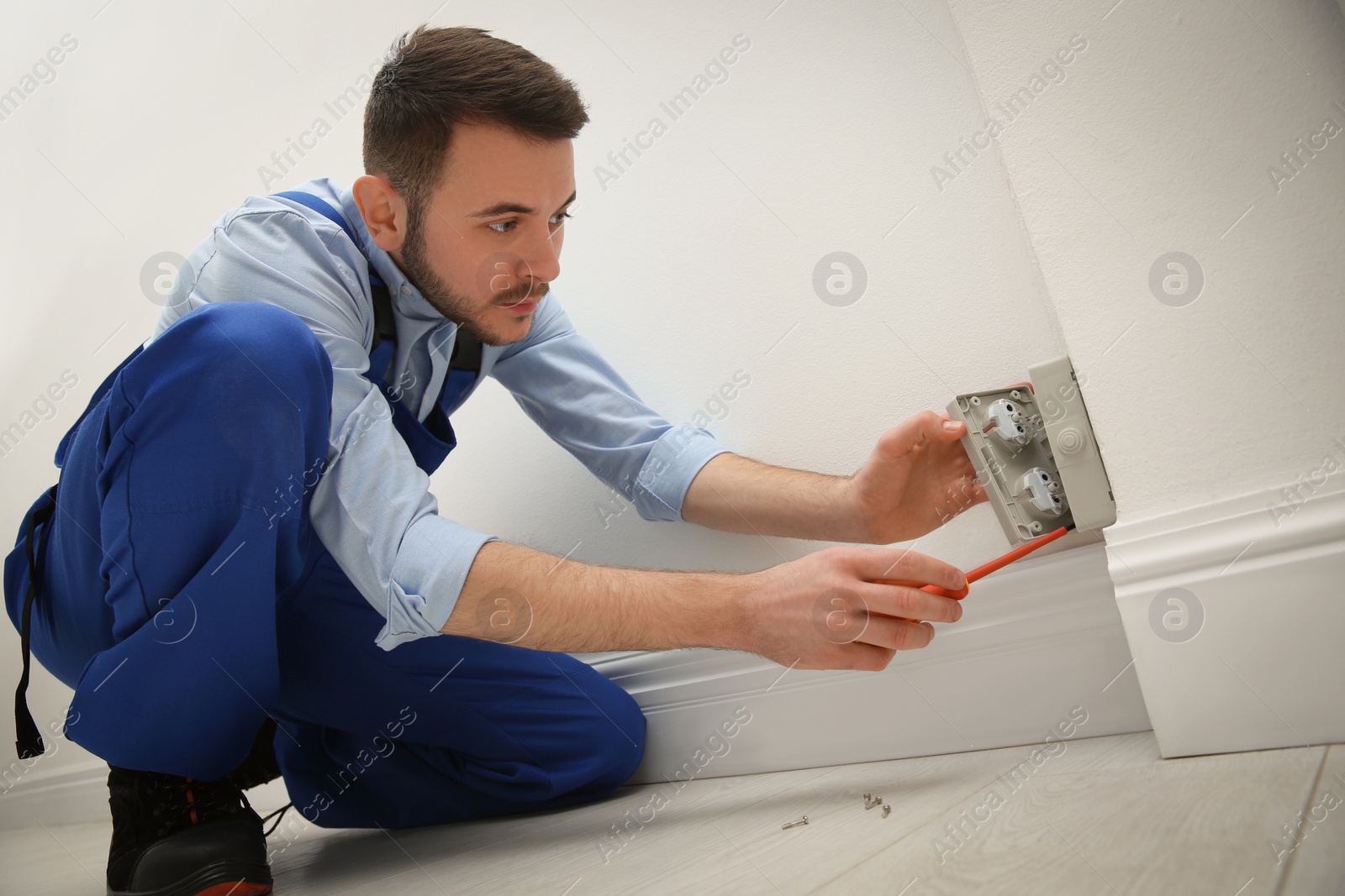 Photo of Electrician with screwdriver repairing power socket indoors