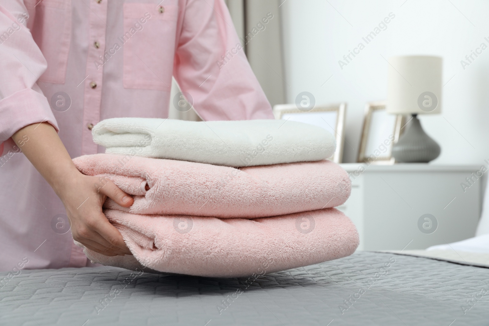 Photo of Woman putting stack of clean towels on bed