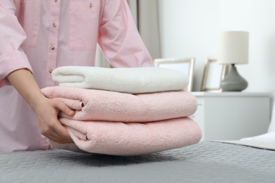 Photo of Woman putting stack of clean towels on bed