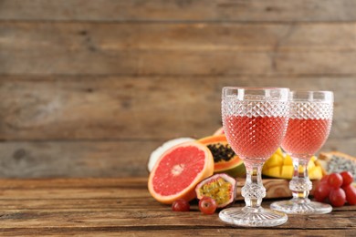 Photo of Delicious exotic fruits and glasses of wine on wooden table, space for text