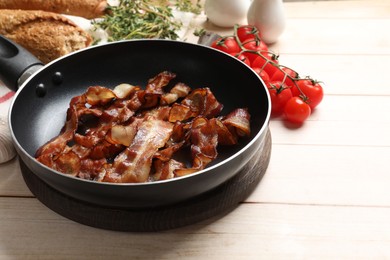 Photo of Delicious bacon slices in frying pan and products on light wooden table, space for text