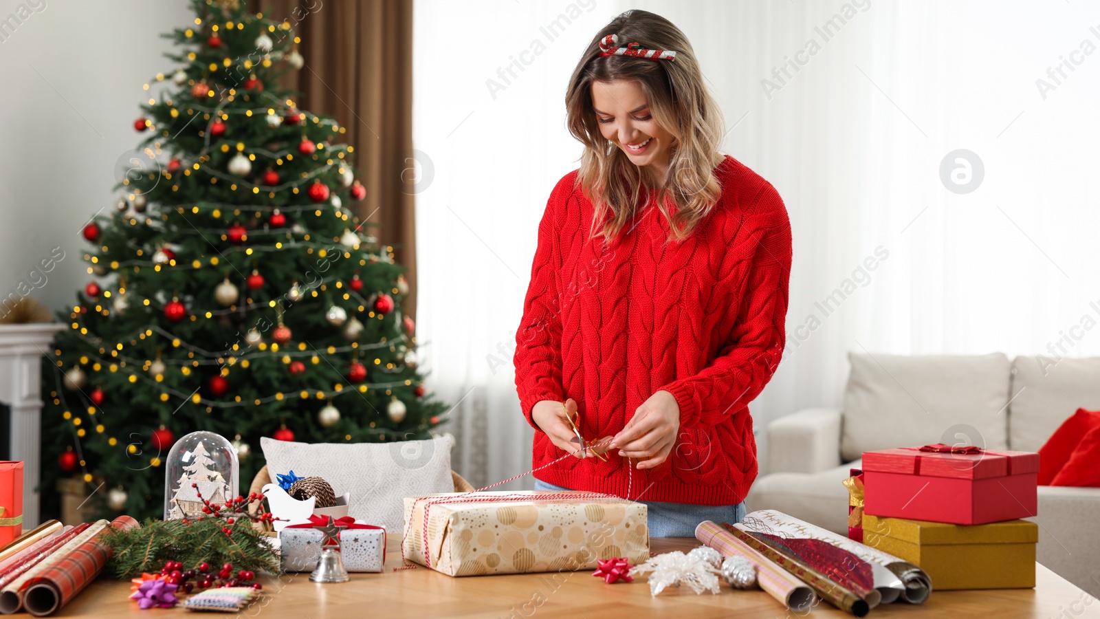 Photo of Beautiful young woman wrapping Christmas gift at home