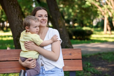 Photo of Happy nanny with cute little boy on bench in park, space for text