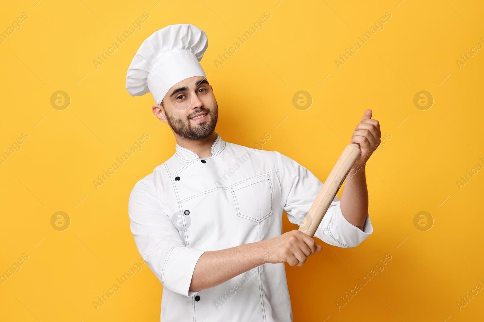 Photo of Professional chef with rolling pin on yellow background