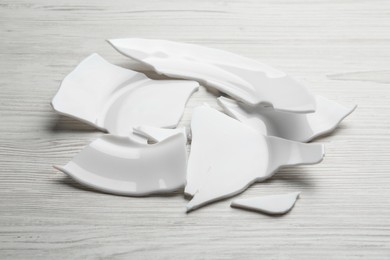 Pieces of broken ceramic plate on white wooden table