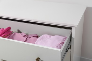 Many folded pink clothes in white chest of drawers indoors, closeup