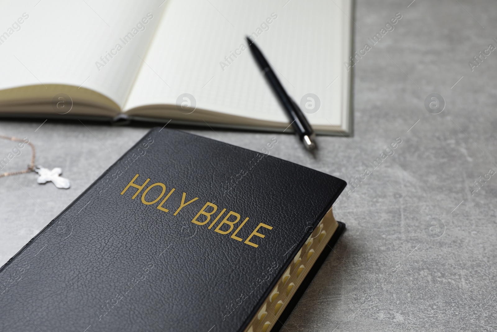 Photo of Old hardcover Bible and notebook with pen on grey table, space for text. Religious book