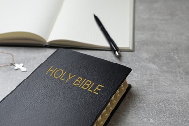 Old hardcover Bible and notebook with pen on grey table, space for text. Religious book