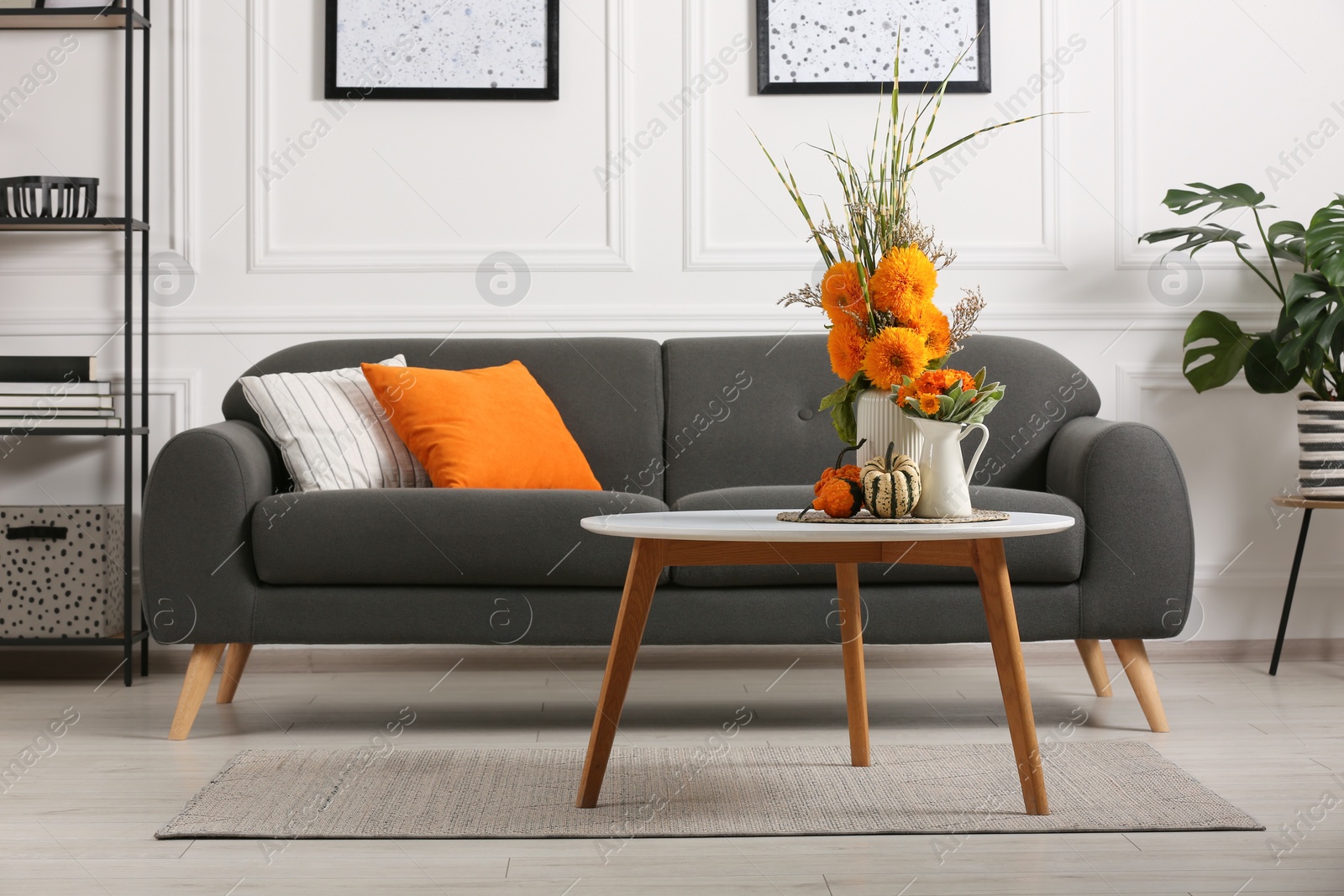 Photo of Beautiful autumn bouquets and pumpkins on coffee table near sofa in room