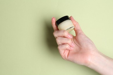 Woman holding jar of cream on green background, closeup. Space for text