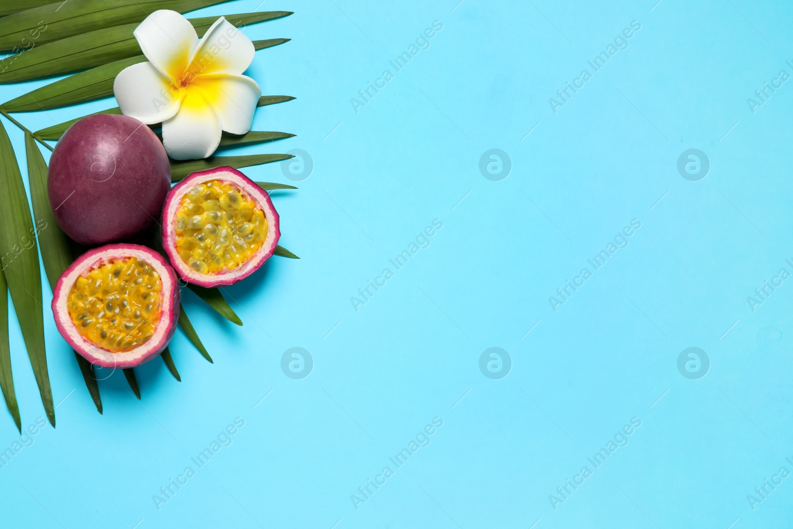 Photo of Passion fruits (maracuyas), flower and palm leaf on light blue background, flat lay. Space for text