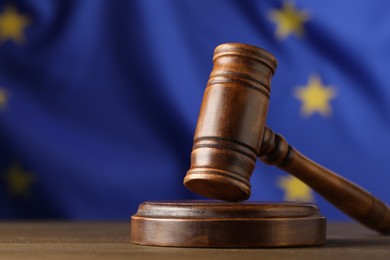 Photo of Judge's gavel on wooden table against European Union flag, closeup. Space for text