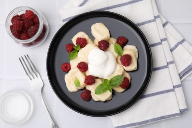Photo of Plate of tasty lazy dumplings with raspberries, sour cream and mint leaves on white tiled table, flat lay