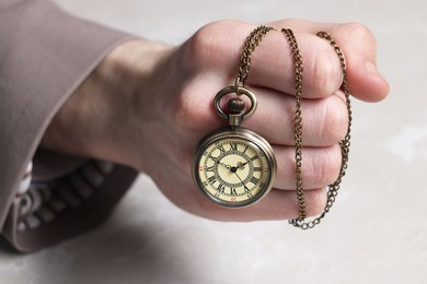 Man holding chain with elegant pocket watch at light marble table, closeup