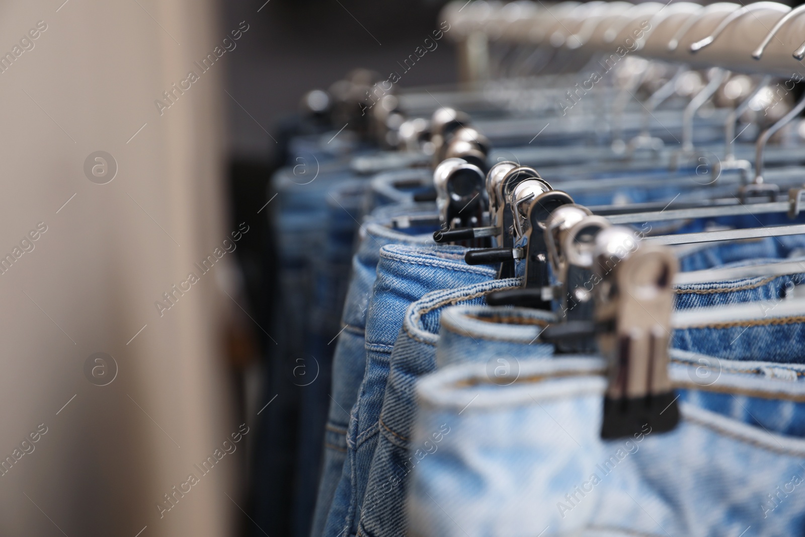 Photo of Hangers with stylish jeans near beige wall, closeup