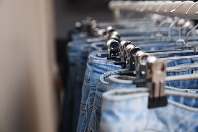 Photo of Hangers with stylish jeans near beige wall, closeup