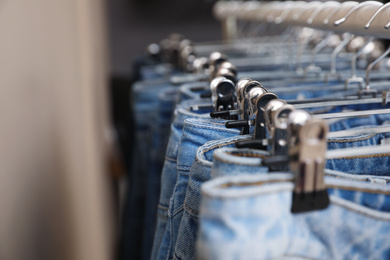 Hangers with stylish jeans near beige wall, closeup