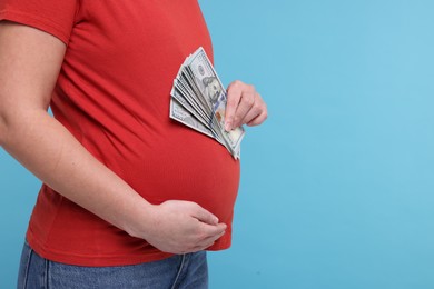 Surrogate mother. Pregnant woman with dollar banknotes on light blue background, closeup. Space for text