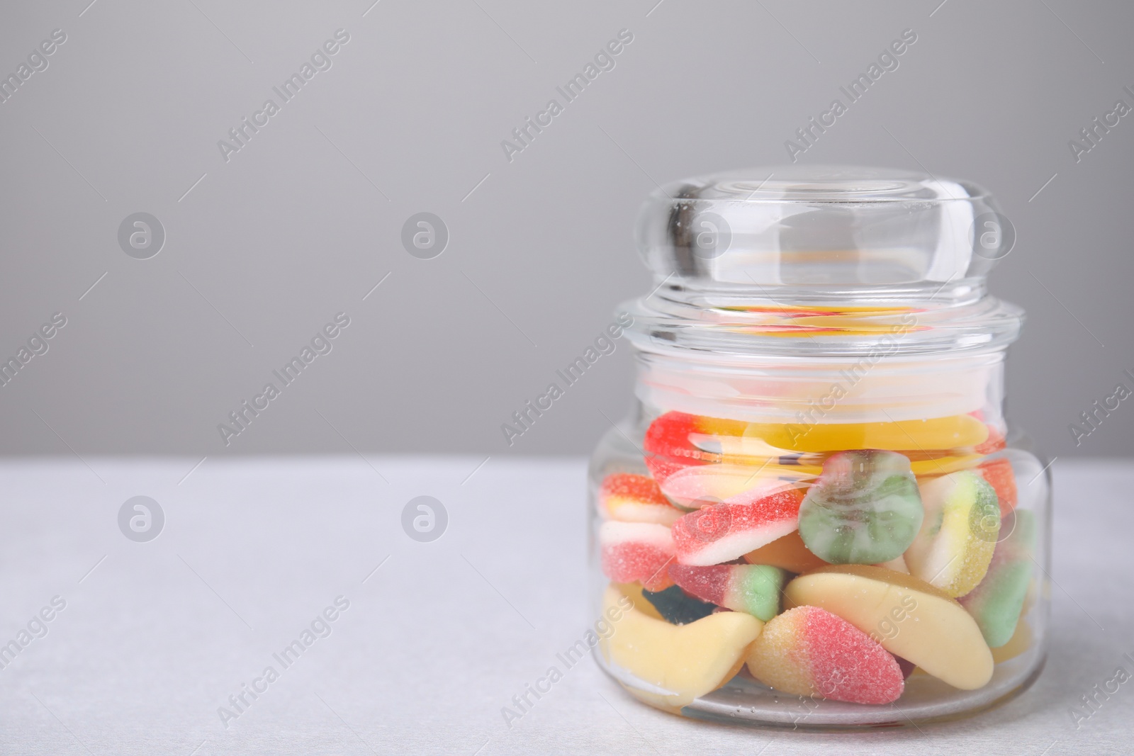 Photo of Tasty jelly candies in jar on light grey table, closeup. Space for text