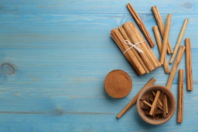 Photo of Aromatic cinnamon sticks and powder on light blue wooden table, flat lay. Space for text