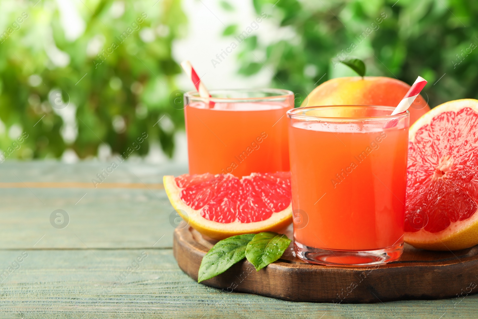 Photo of Glasses of delicious grapefruit juice on wooden table against blurred background, space for text